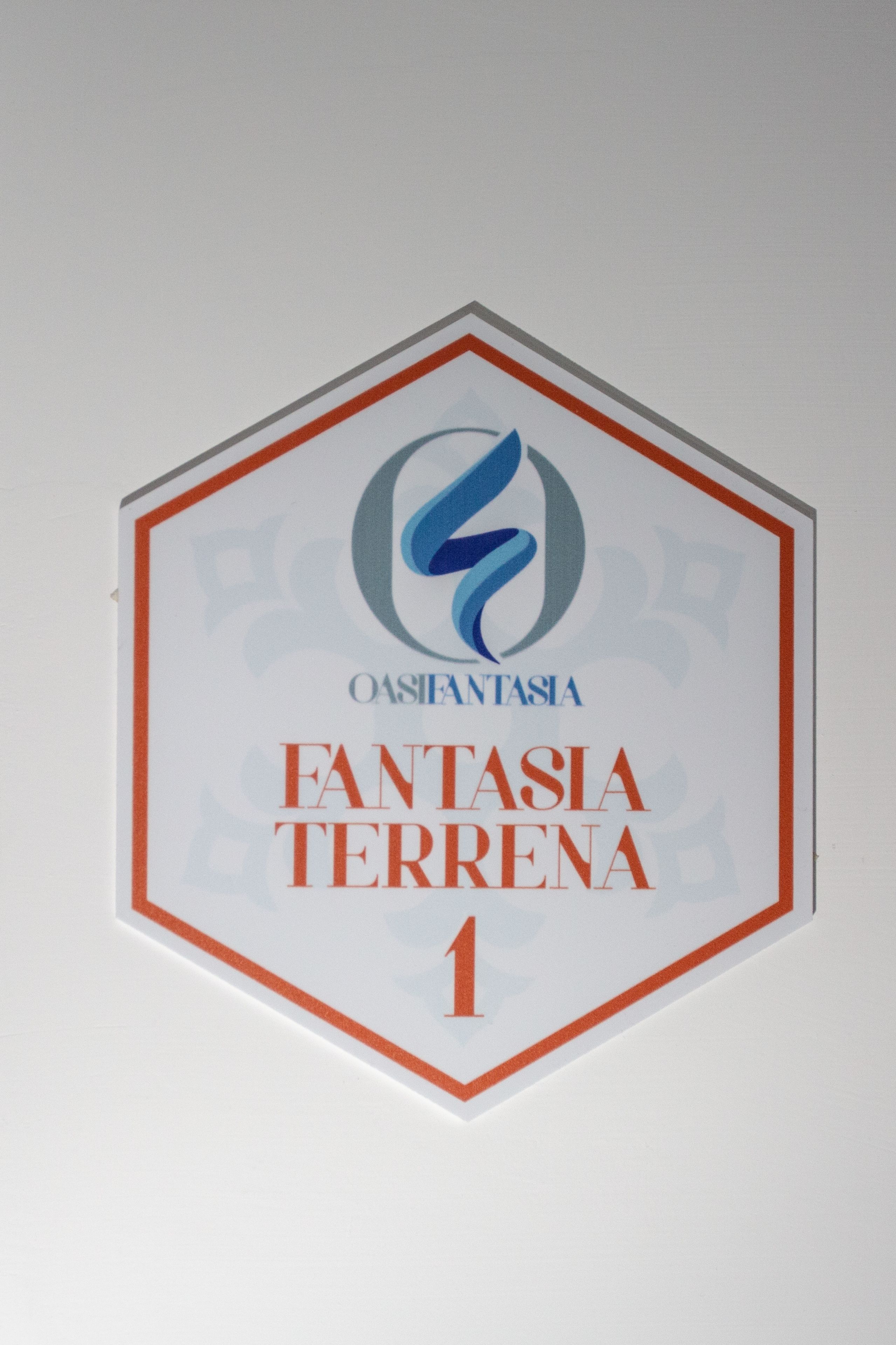 A hexagonal sign with the text "OASIENTASIA" and "FANTASIA TERRENA 1".