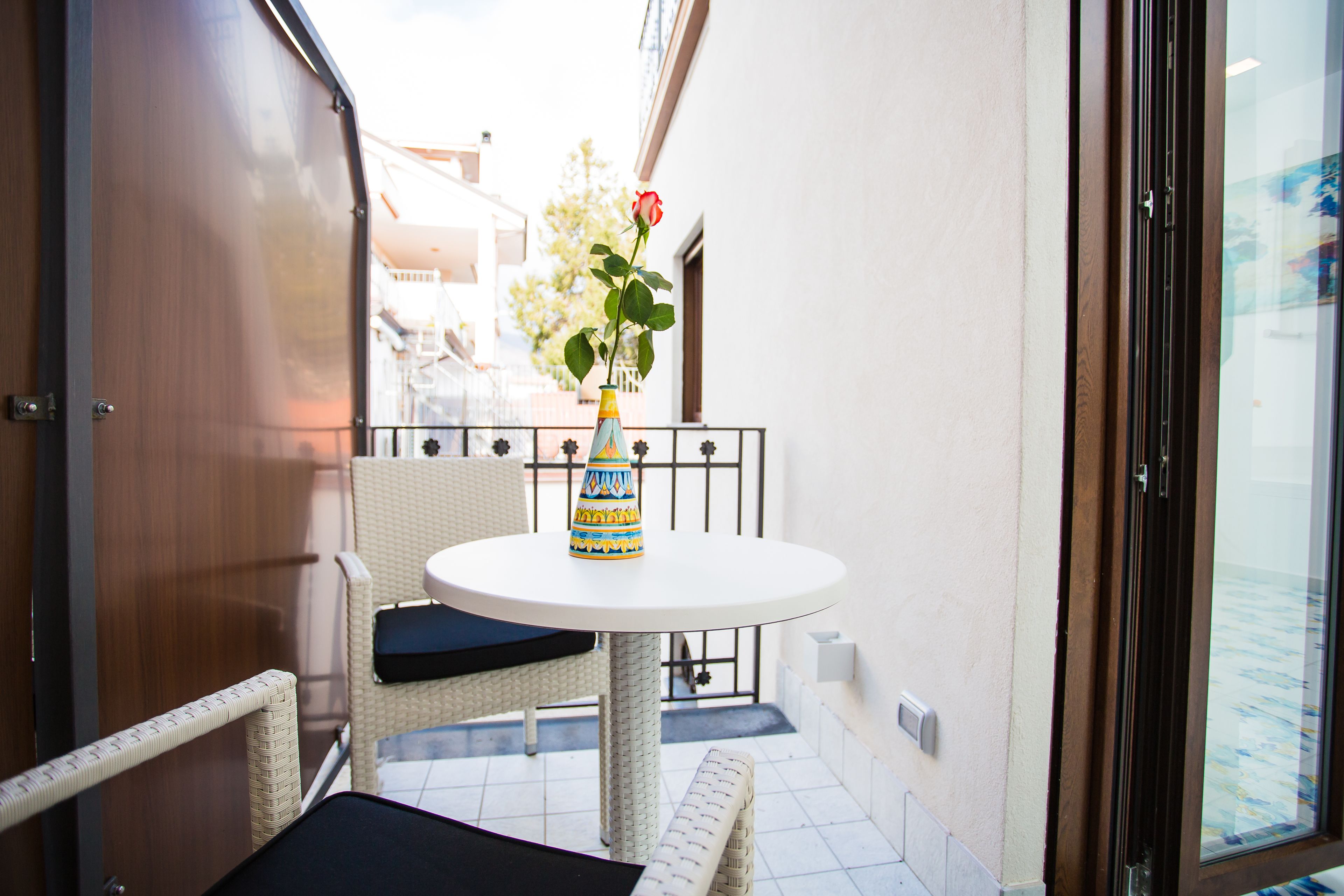 A small outdoor seating area with a round table and wicker chairs, a potted plant, and a view of the street.