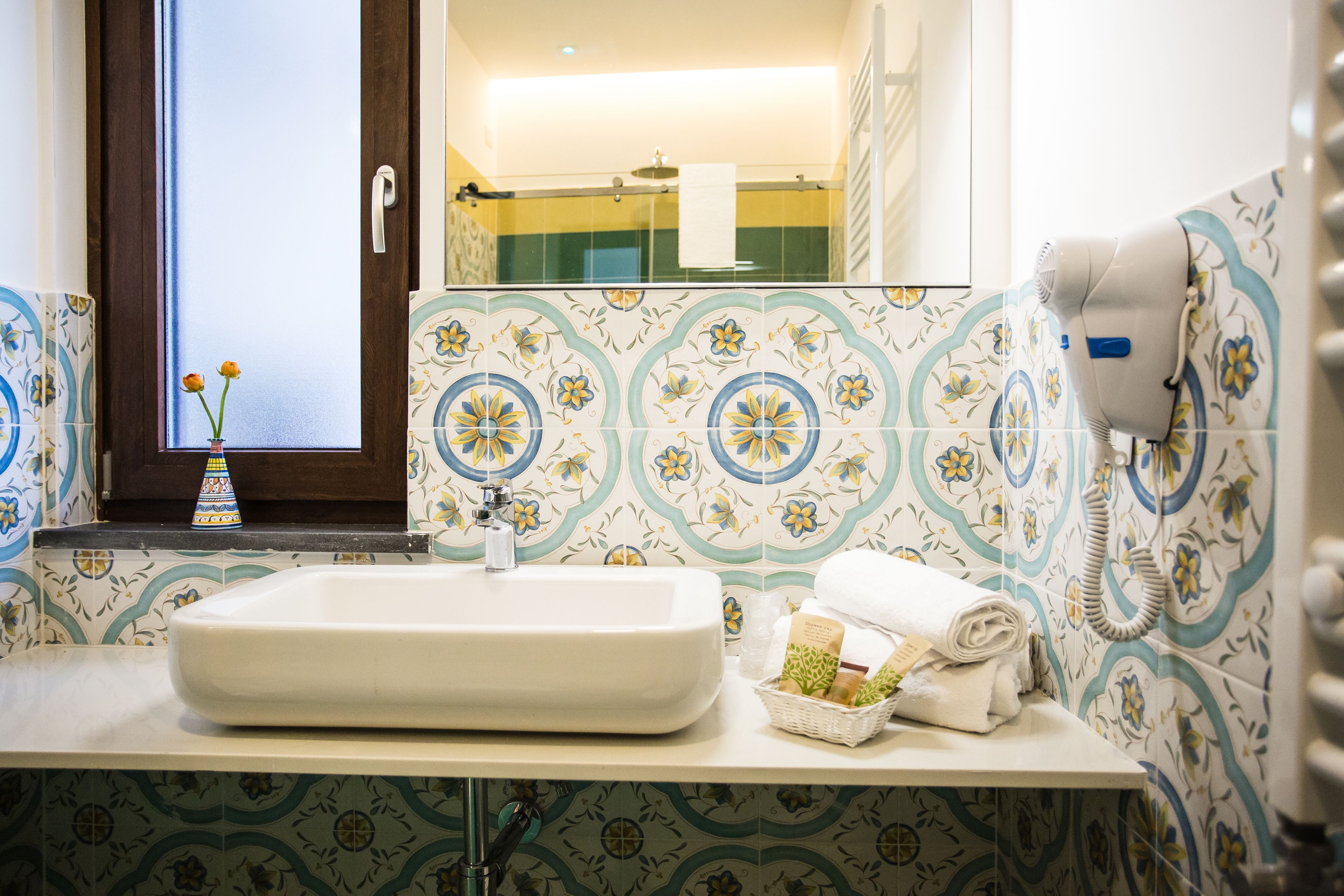 A bathroom with a large sink, a hairdryer, and a window with flowers.