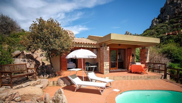A pool area with lounge chairs and a table, surrounded by rocks and vegetation. - Sole 1 (Trinità d'Agultu e Vignola)