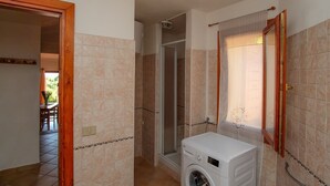 Une salle de bain avec des carreaux de couleur beige, une douche, un lave-linge et un miroir.