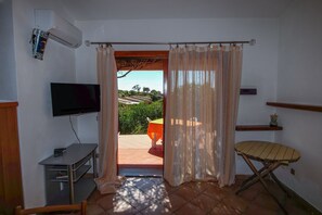 Une pièce avec un téléviseur, une petite table, une chaise et une vue sur un jardin, visible par une porte.
