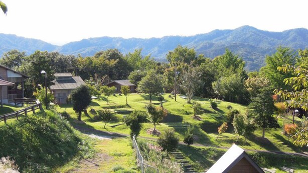 Paisagem rural com casas, árvores e montanhas ao fundo.
