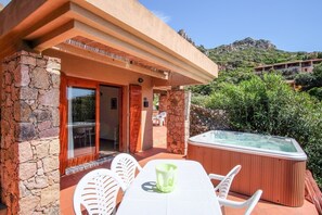 A villa with a stone exterior, a wooden door, a glass door leading to a patio, a hot tub, and a table with chairs. - Sole 3 (Trinità d'Agultu e Vignola)