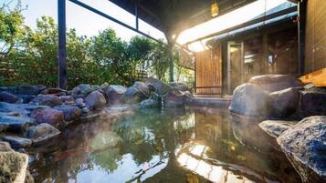 A hot spring area with rocks, a wooden structure, and a building in the background.