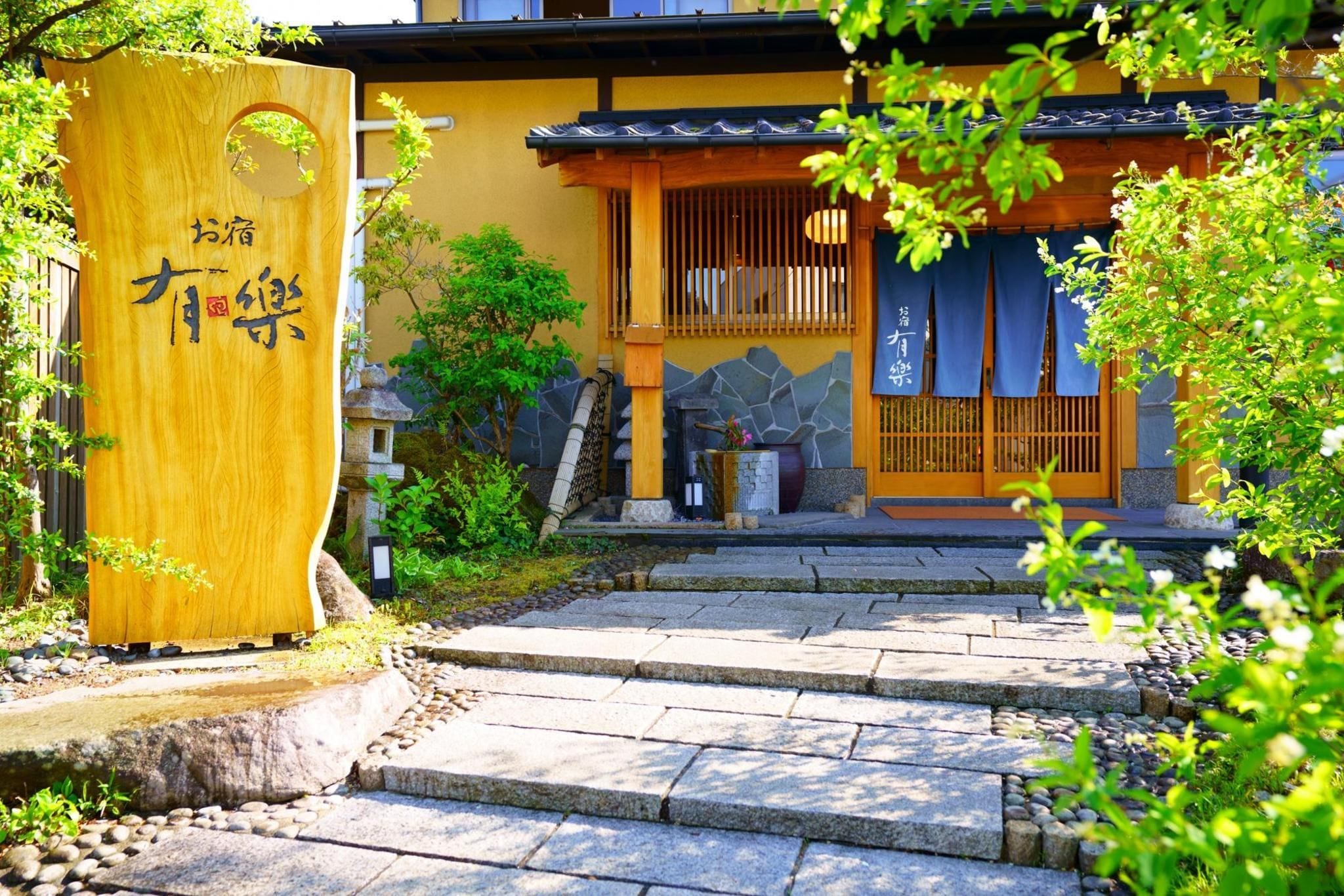 A traditional Japanese building with a wooden entrance gate, stone steps, and a small garden area.