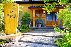 A traditional Japanese building with a wooden entrance gate, stone steps, and a small garden area.