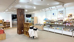 A spacious retail store with wooden shelves, a central display table, and a variety of products on shelves. - Kitamura Onsen Hotel (Iwamizawa)
