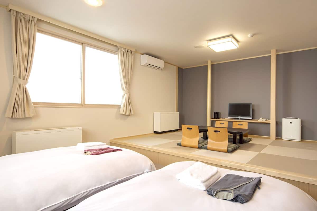 Habitación de hotel con dos camas, un escritorio con computadora y parlantes, un televisor y un equipo de aire acondicionado.