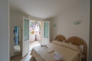 Une chambre à coucher comprenant un lit, deux tables de chevet et une porte donnant sur un balcon.