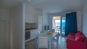A compact living space with a kitchenette, a dining area, and a red couch. - Green 2 (Trinità d'Agultu e Vignola)