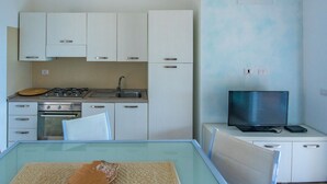 A compact kitchen with white cabinets, a gas stove, an oven, and a sink. A television is placed on a small table next to the cabinets. - Green 2 (Trinità d'Agultu e Vignola)