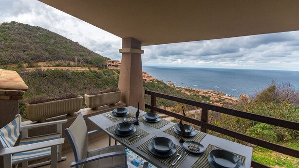 An outdoor dining area with a table set for four, overlooking a coastal landscape with a view of the sea and hills. - Green 2 (Trinità d'Agultu e Vignola)