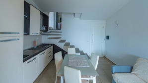 A compact kitchen with a dining area, a staircase, and a sofa. - Green 3 (Trinità d'Agultu e Vignola)