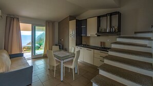 A compact living space with a kitchenette, a dining area with a table and chairs, and a sofa. There is a staircase leading to an upper level. - Green 3 (Trinità d'Agultu e Vignola)