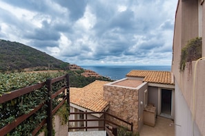 Une vue sur la côte, depuis un balcon doté d’un mur en pierre et d’un toit en tuiles, donnant sur la mer et un paysage vallonné.