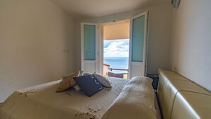 A bedroom with a bed, pillows, and a view of the sea through an open door. - Green 3 (Trinità d'Agultu e Vignola)