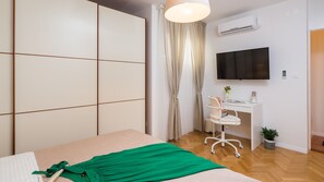 A bedroom with a bed, a desk with a chair, a TV, an air conditioner, and a potted plant. - Sun Spalato Garden (Split)