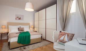 Relax in a serene space with a neatly made bed, a cozy reading area, and a large window with sheer curtains.