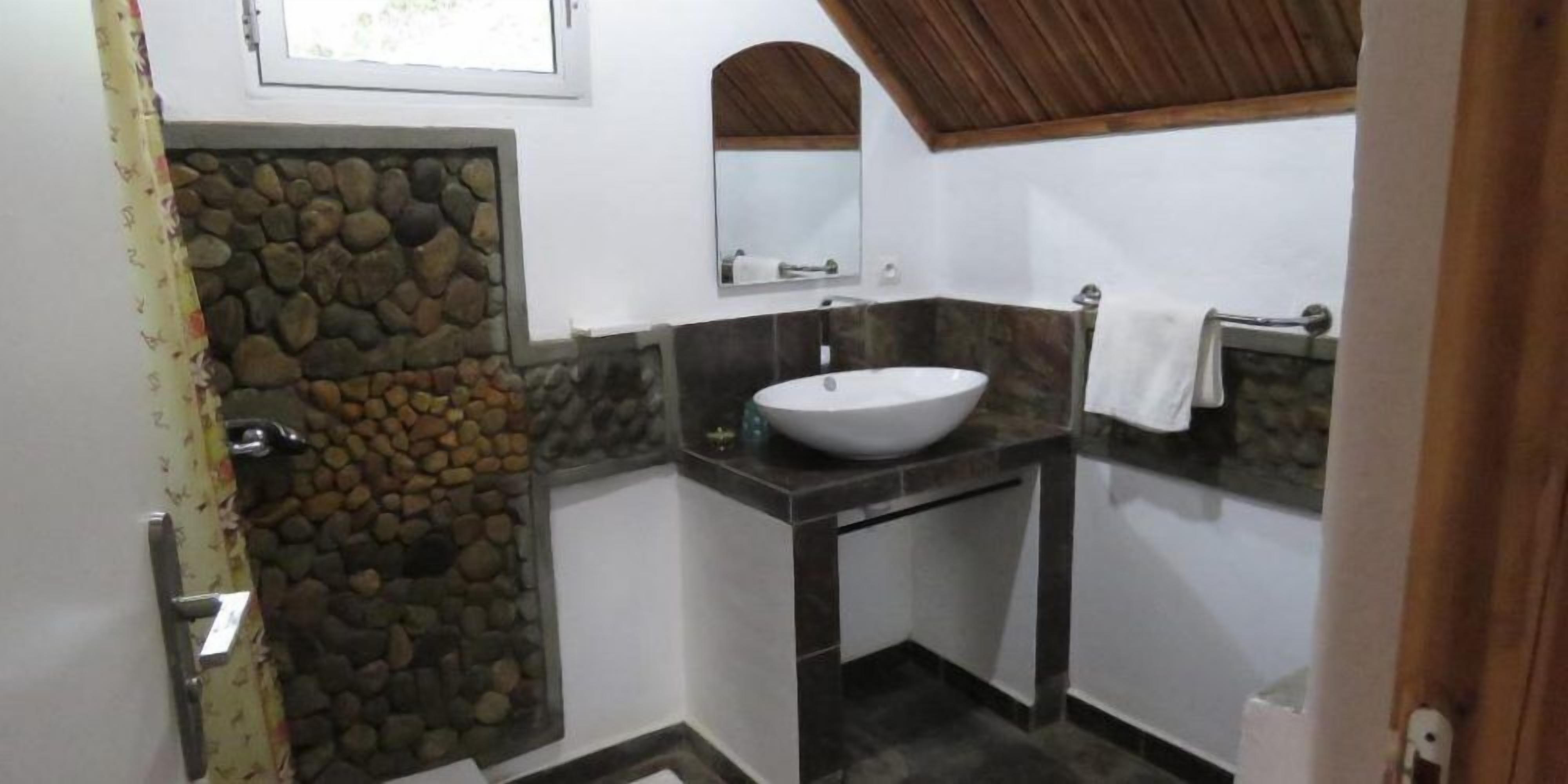 Un baño con pared de piedra, lavamanos blanco y espejo.