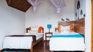 A room with two beds, wooden headboards, a nightstand with a lamp, and a wall with leaf patterns. - Karibotel (Antananarivo)