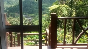 A view from a balcony with a wooden railing, overlooking a lush green landscape with hills and trees. - Karibotel (Antananarivo)
