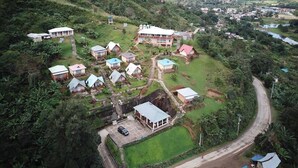 An aerial view of a hillside resort with multiple bungalow-style accommodations, a central building, and a winding road. - Karibotel (Antananarivo)