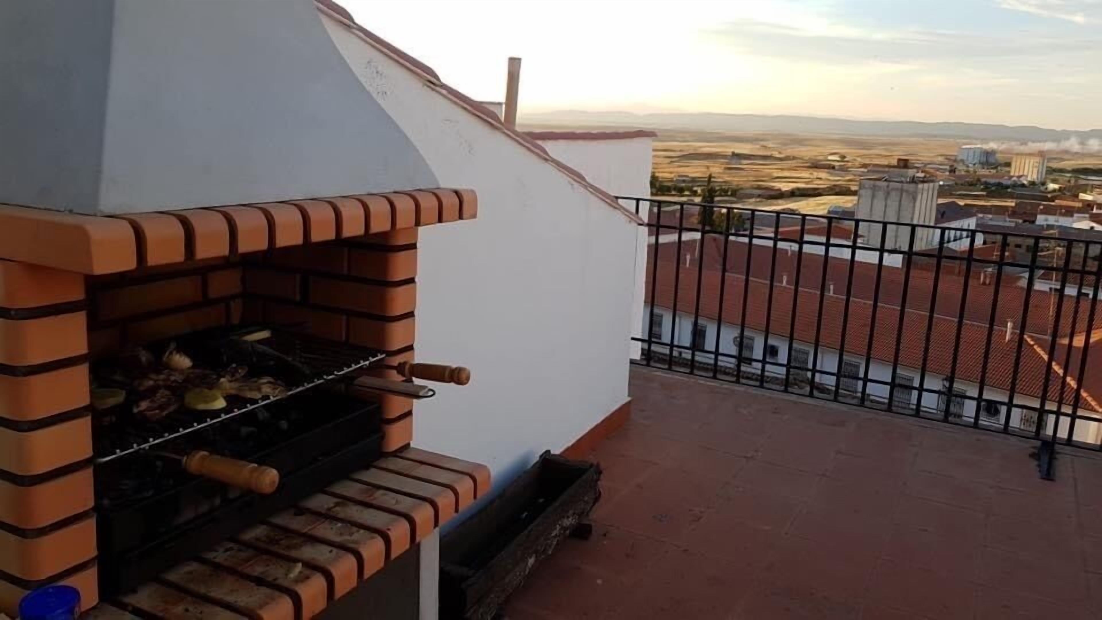 A rooftop with a brick barbecue grill and a view of the surrounding landscape.