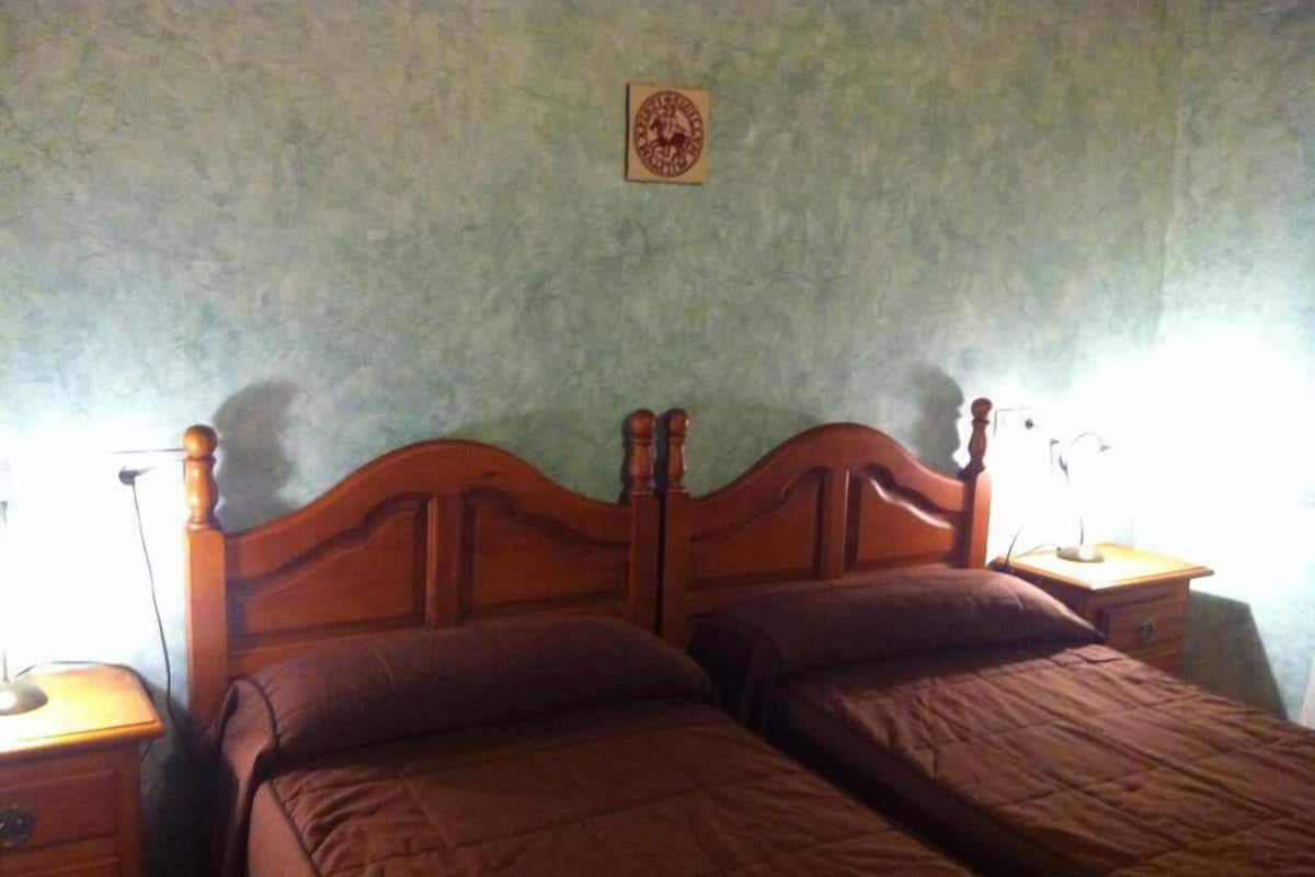 A bedroom with a wooden bed frame, two pillows, and a nightstand with a lamp.