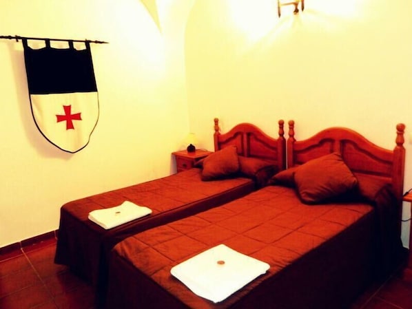 A room with two single beds, each with a pillow and a laptop on the bed. There is a nightstand with a lamp between the beds. - La Casa de los Templarios (Puebla de Alcocer)