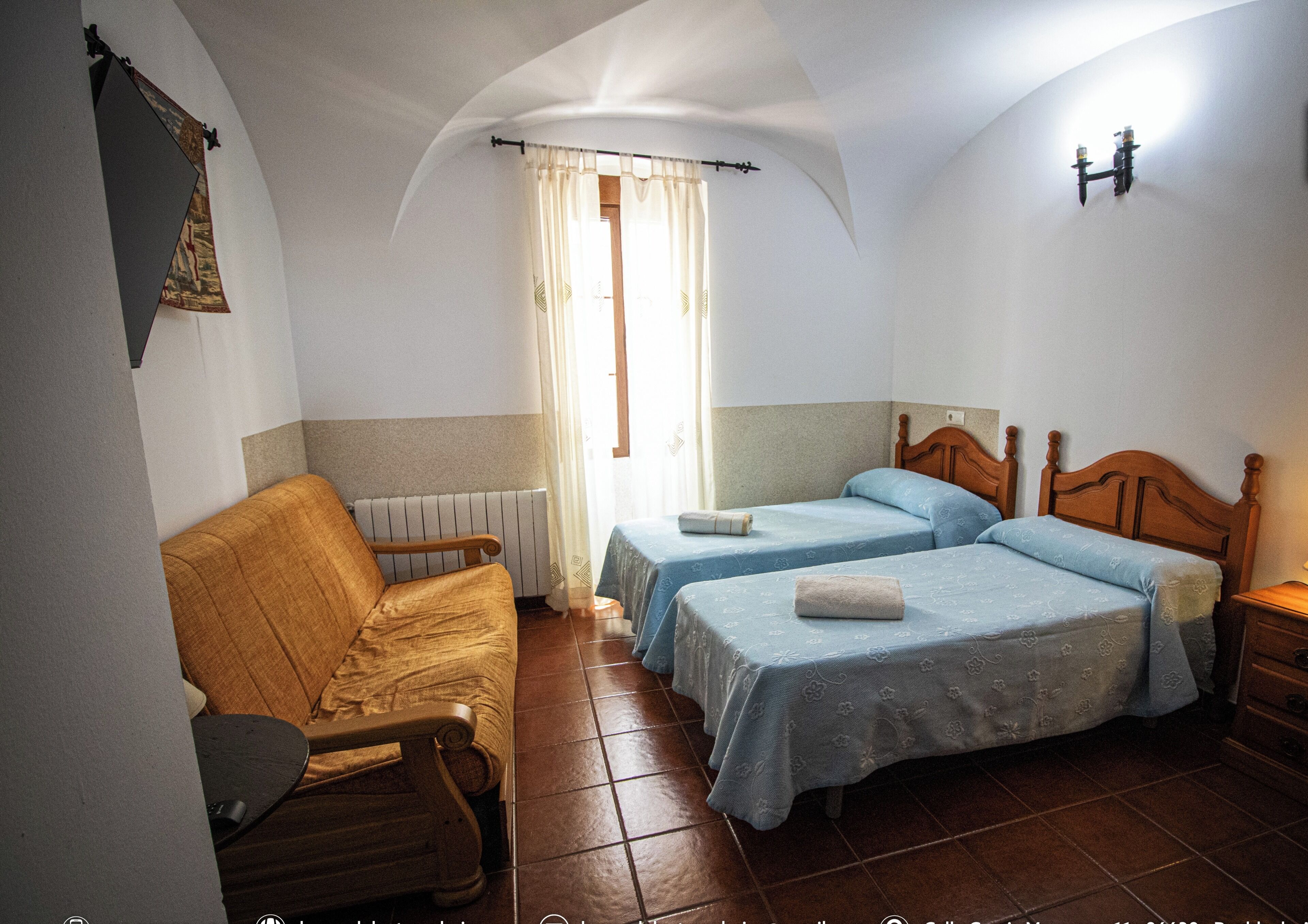 Una habitación con dos camas, un sofá, un radiador y una ventana con cortinas.