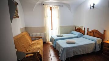Una habitación con dos camas, un sofá, un radiador y una ventana con cortinas.
