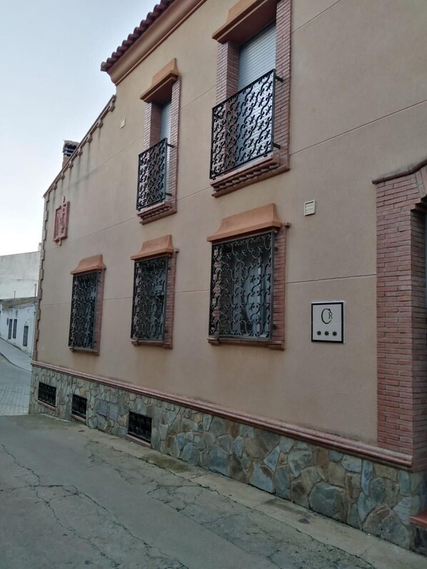 Un edificio con fachada color crema, varias ventanas con rejas de hierro decorativas y una base de piedra.
