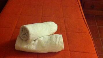 Una cama con una colcha naranja y dos toallas blancas dobladas encima.