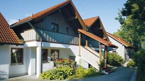 Ein zweistöckiges Haus mit einem steilen Satteldach, einer Holztreppe und einem kleinen Gartenbereich mit Pflanzen und Blumen.