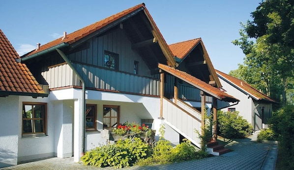 A two-story house with a steeply pitched roof, a wooden staircase, and a small garden area with plants and flowers.