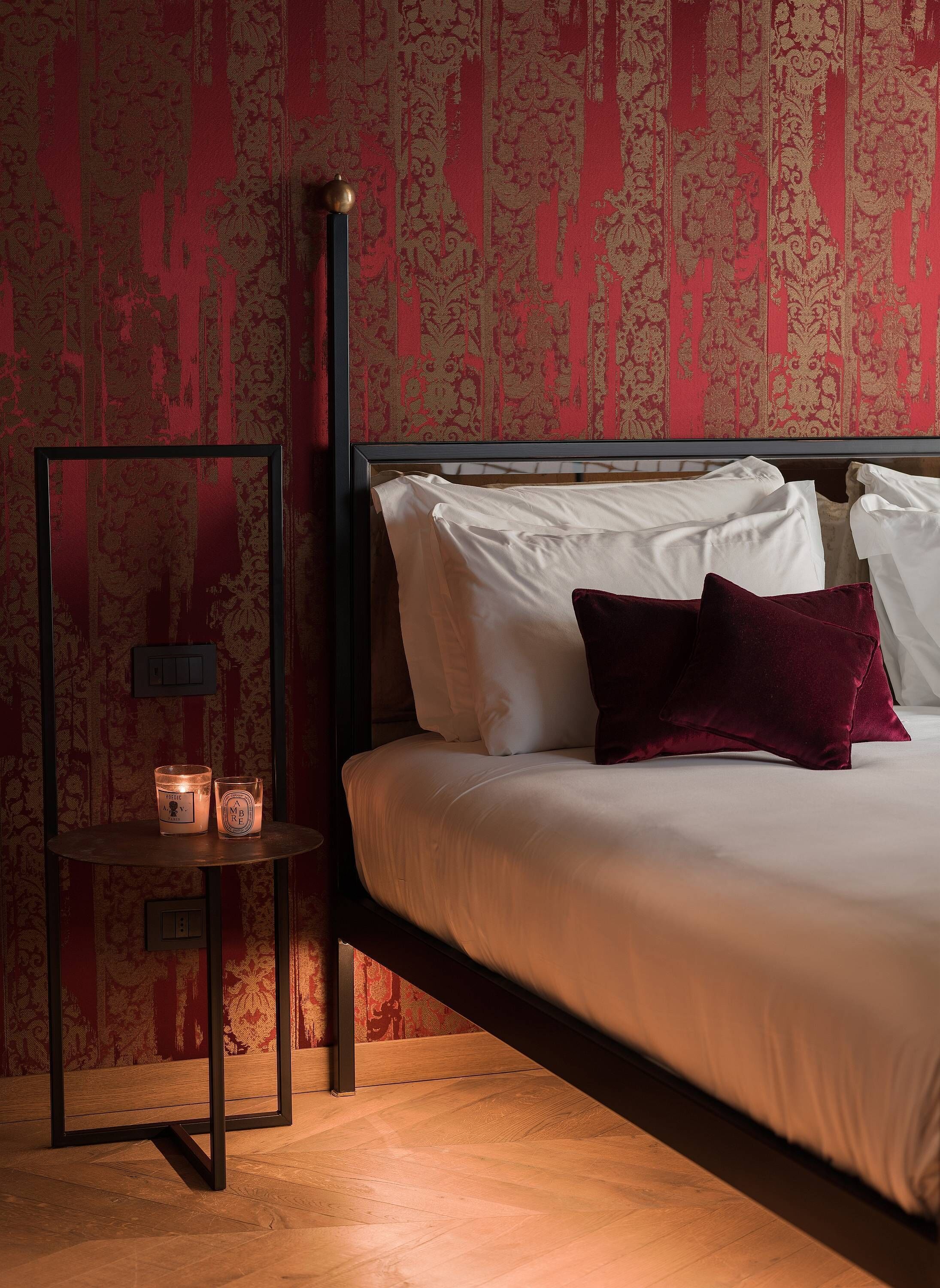 Ein Schlafzimmer mit einem Bett, Kissen, einem Nachttisch mit Kerzen und floraler Tapete.