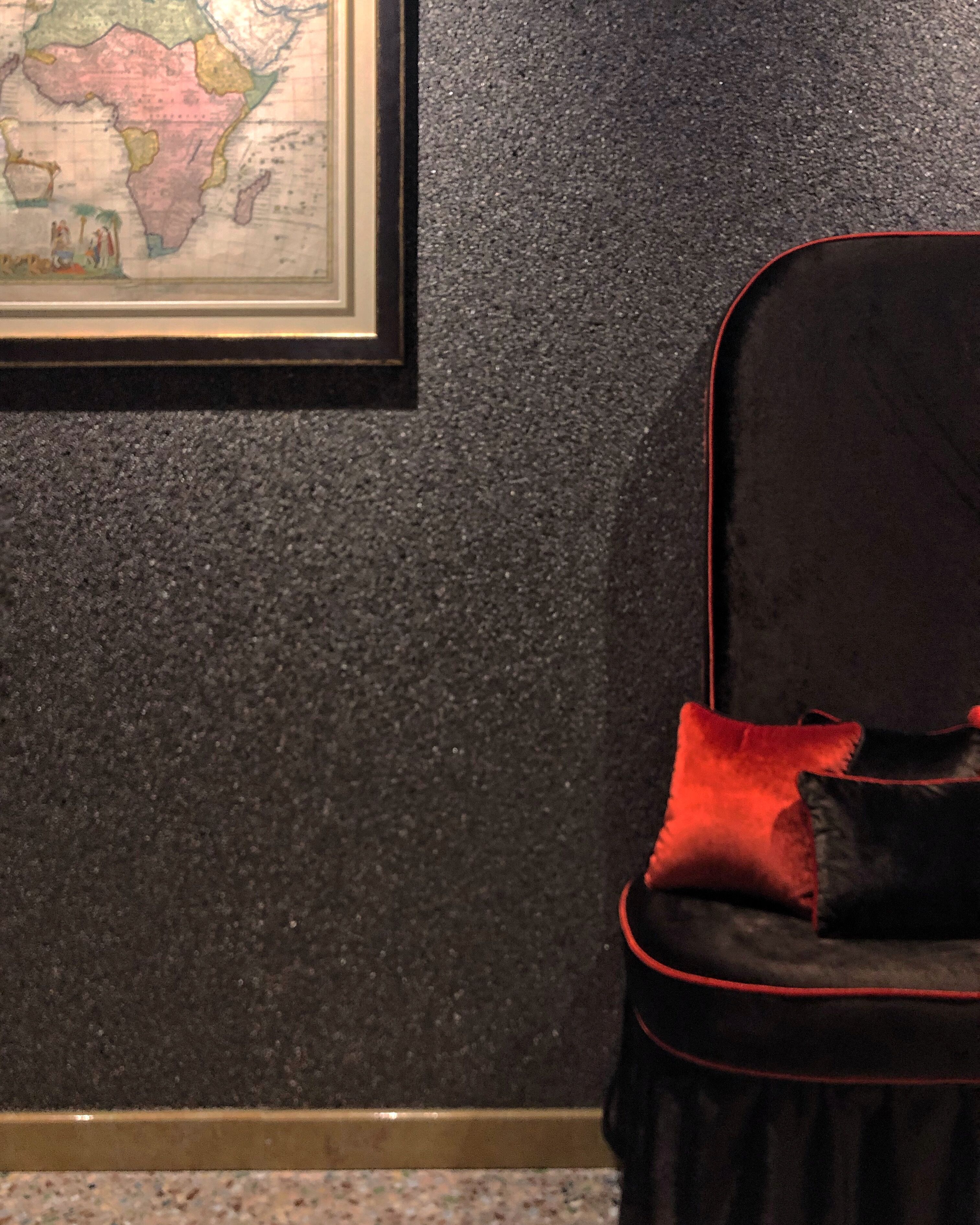 A room with a dark textured wall, a framed map, and a black chair with red trim.
