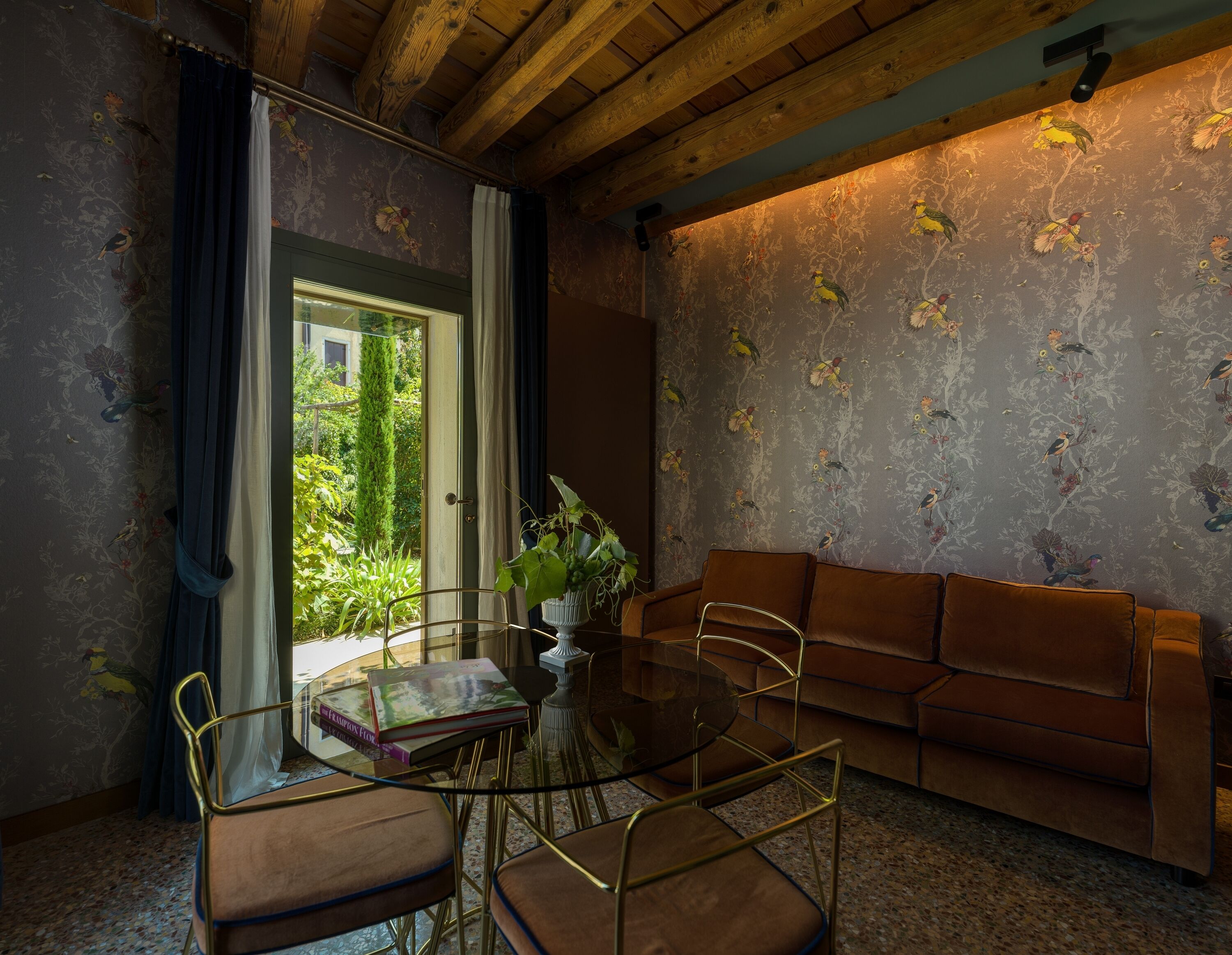 Una habitación con una mesa de vidrio, un sofá marrón y papel tapiz con motivos florales.