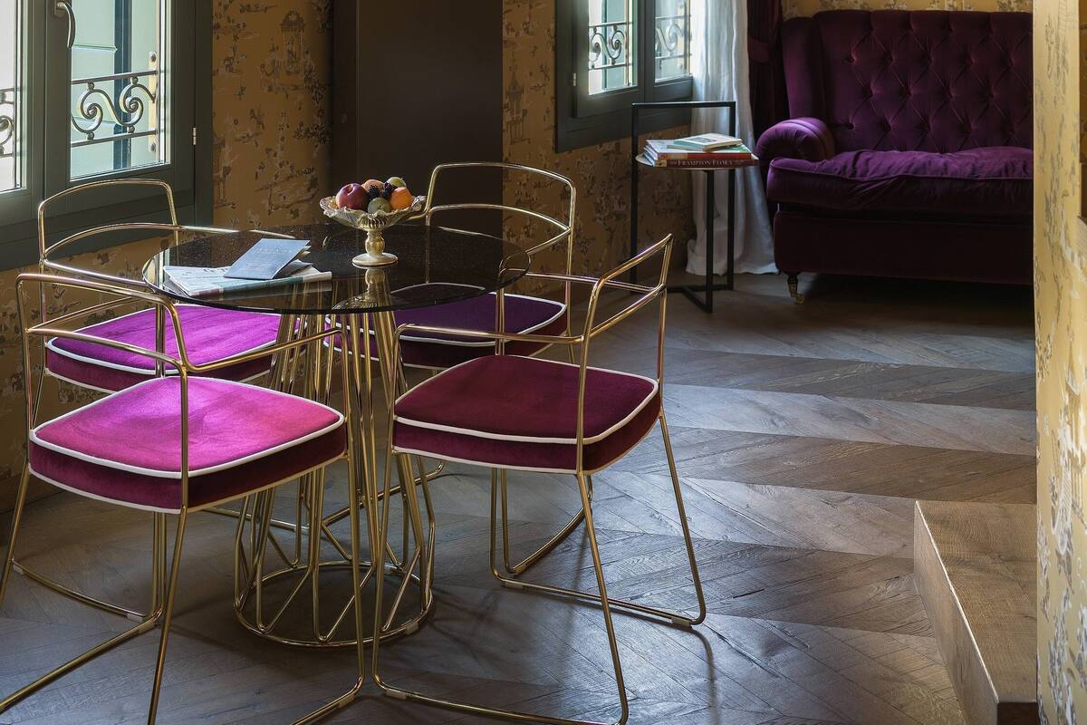 A room with a dining table and chairs, a purple sofa, and patterned wallpaper.