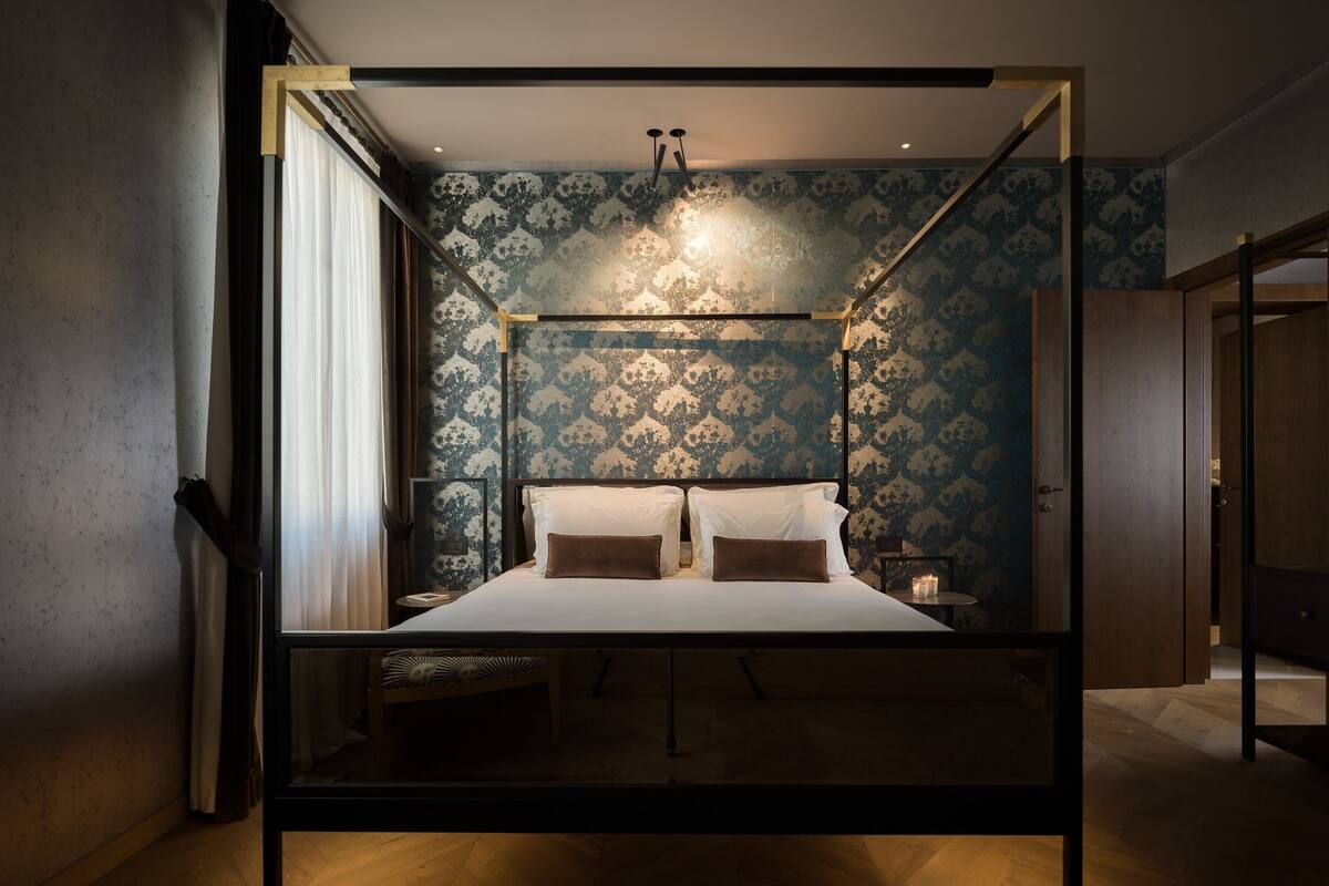 A modern bedroom with a four-poster bed, a nightstand, and a bedside table with a candle.