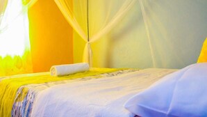 Een bed met een witte dekbedovertrek, een opgerolde witte handdoek en een geel accentmuur.