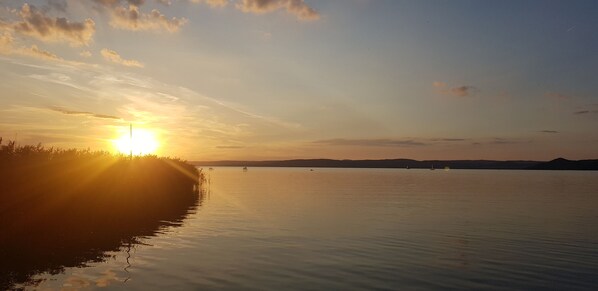 A calm lake at sunset with boats and distant hills.