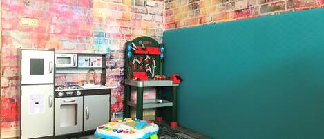 A play kitchen with a bear, a toy table, and a colorful wall.