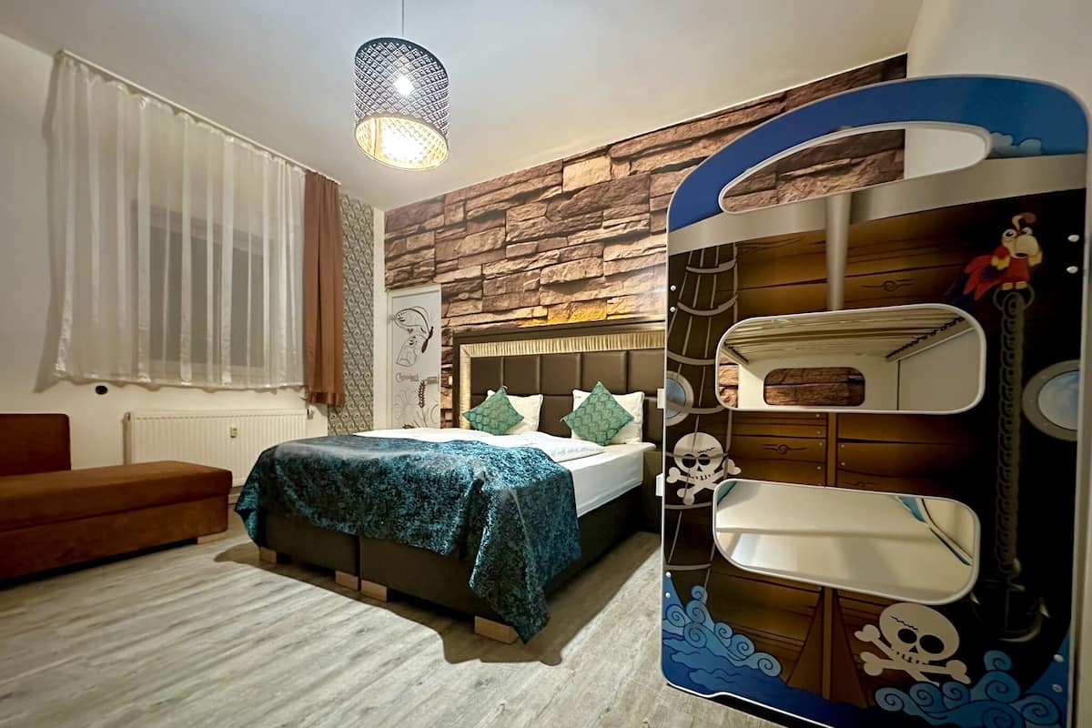 Un dormitorio con cama, cabecera de madera, ventana con cortinas, lámpara colgante y pared con textura de madera.