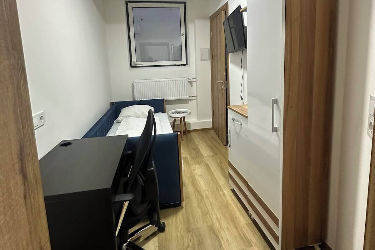Una habitación pequeña con cama, escritorio, silla, televisor y armario.