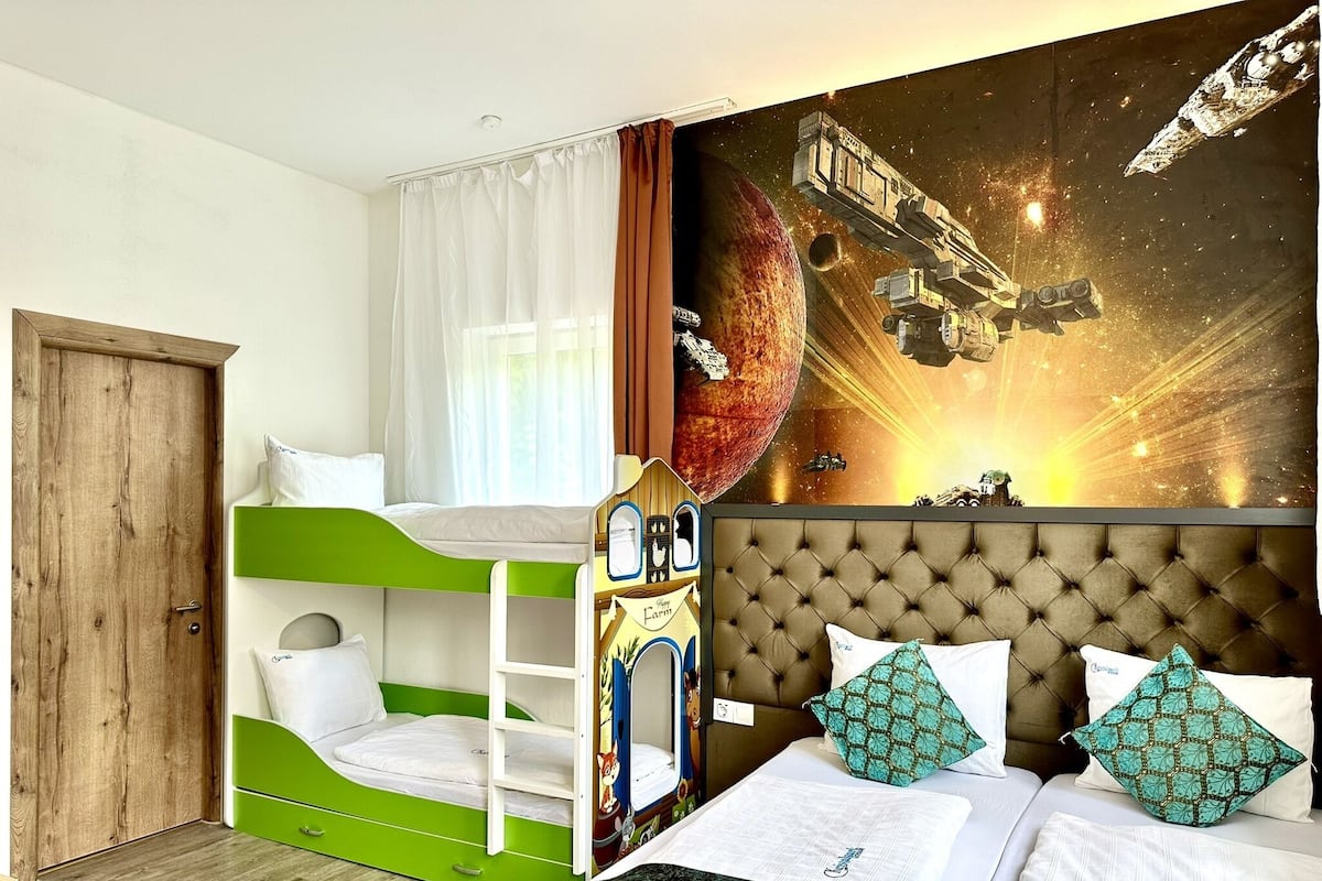 Una habitación con literas, un mural grande con temática espacial y una puerta de madera.
