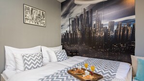 A hotel room with a bed featuring a cityscape mural, a breakfast tray with croissants and juice, and a framed picture on the wall. - Sun Spalato Art (Split)