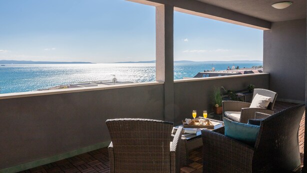 A balcony with wicker furniture, a table with a tray of food and drinks, and a view of the sea and distant land. - Sun Spalato Art (Split)