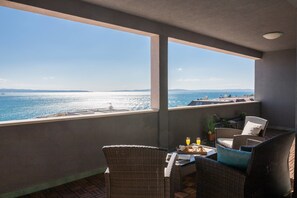 A balcony with wicker furniture, a table with a tray of food and drinks, and a view of the sea and distant land. - Sun Spalato Art (Split)